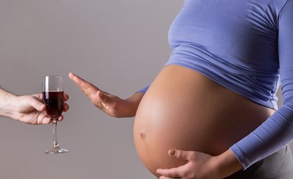 A pregnant woman waves off a glass of red wine.